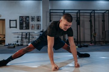 A male athlete stretches intensely in a dimly lit gym environment, preparing for training.