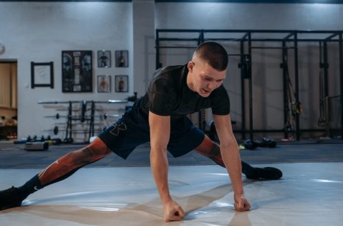 A male athlete stretches intensely in a dimly lit gym environment, preparing for training.